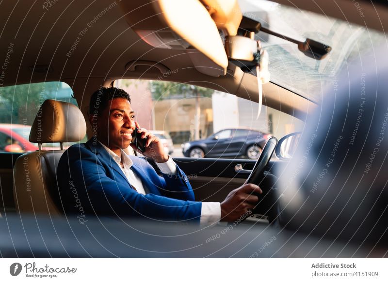 Smiling ethnic businessman talking on smartphone in car drive happy communicate positive urban formal young african american black male entrepreneur elegant