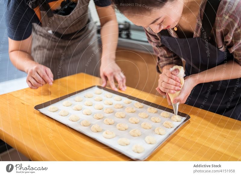 Young bakers piping pastries together in kitchen couple bakery home teamwork pastry piping bag pipe pastry bag batter dough fun explain cheerful small business