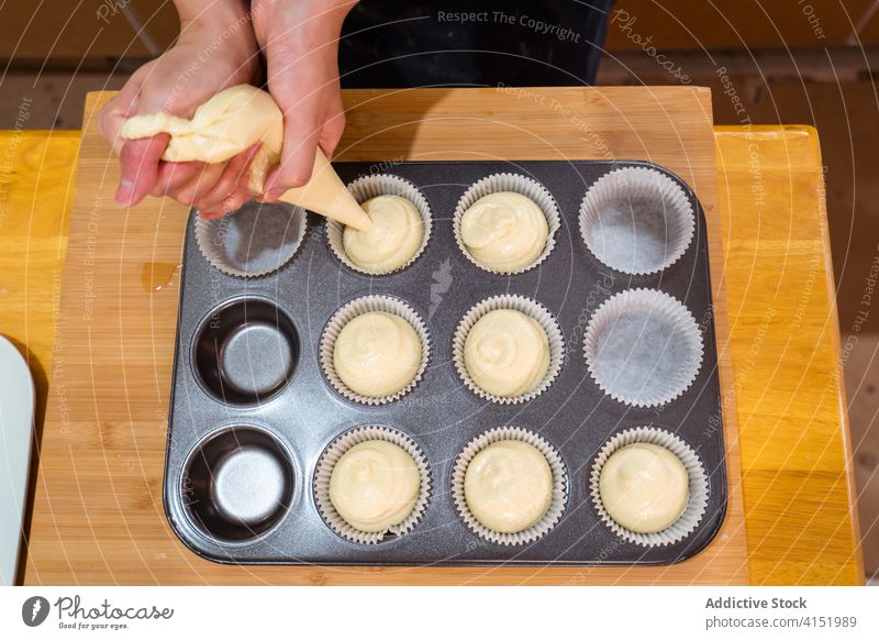 Faceless baker filling baking cups muffin batter form pour cupcake pastry bag piping bag dough delicious bakery cuisine gourmet kitchen sweet dessert recipe