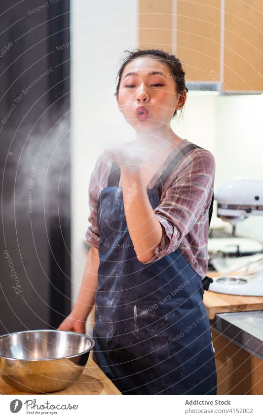 Playful baker blowing flour dust woman playful air fun happy home kitchen apron powder cheerful table joy pastry ingredient domestic cook prepare culinary
