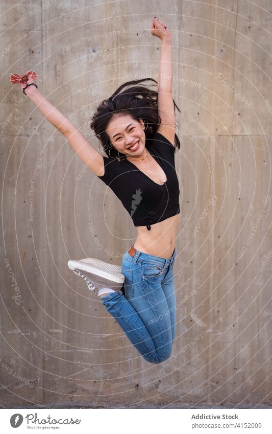 Cheerful ethnic woman jumping in city victory celebrate win triumph delight cheerful achieve joy excited female asian success smile happy glad optimist