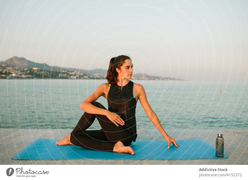 Flexible woman in Half Lord of the Fishes pose lord of the fishes pose ardha matsyendrasana yoga flexible stretch sea pier female body evening seascape tranquil