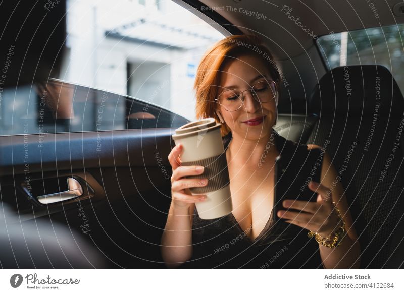 Content female entrepreneur with coffee and smartphone in car businesswoman taxi commute work using modern cellphone mobile connection message surfing smile