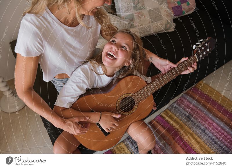 Girl looking and smiling at a woman who's teaching her to play guitar music education learning lesson playing instrument musician performance pupil study class