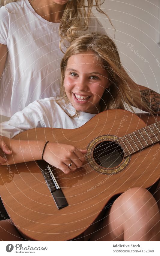 Portrait of a blonde girl playing guitar while smiling on camera with a woman sitting with he vertical music teacher education learning student teaching lesson