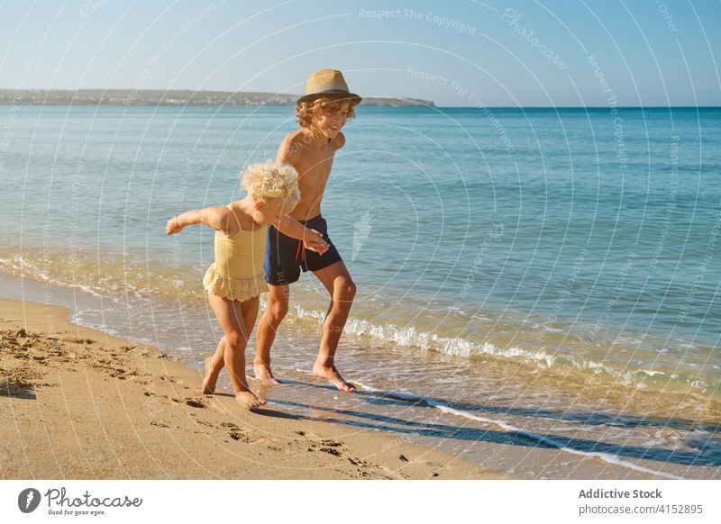 Two children in swimsuits holding hands running on the seashore together primary sister trust affectionate sharing feeling moment brother jump touch protective