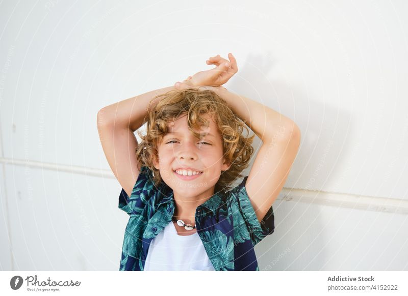 Boy in summer clothes leaning against a wall while is facing the camera vertical children confident arm posing positive shirt model expression standing youth
