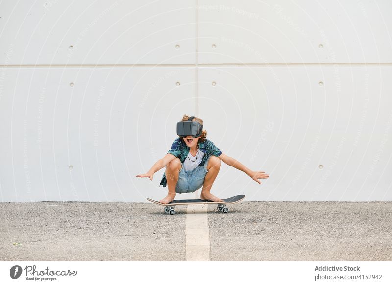 Boy in summer clothes skating on skateboard wearing virtual reality glasses reaction touching gesturing optical dimensional experience headset imagination