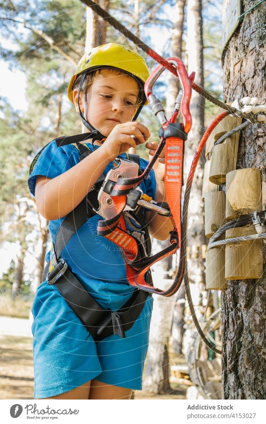 Cute boy in adventure park equipment carabine safety harness entertain having fun weekend summer rope protect helmet extreme activity hobby active nature modern