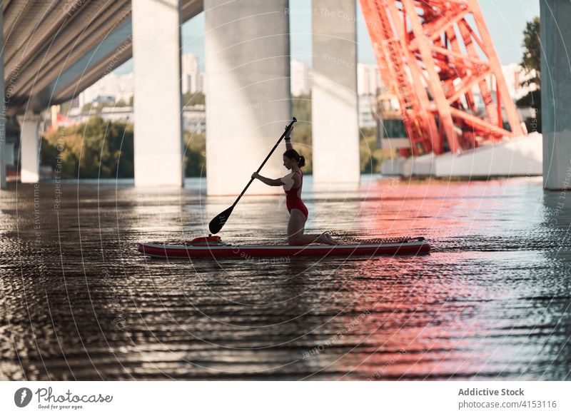 Female surfer swimming on paddle board paddleboard woman row surfboard river bridge city female water summer activity sport cityscape hobby equipment swimsuit