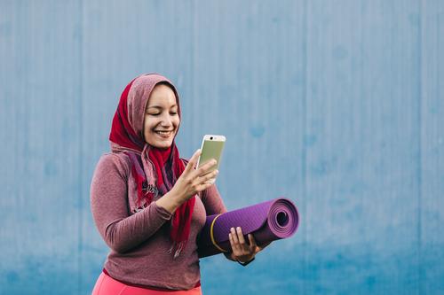 Smiling ethnic sportswoman using smartphone in city browsing hijab muslim smile mat female arab training mobile street sportswear fitness internet lady content