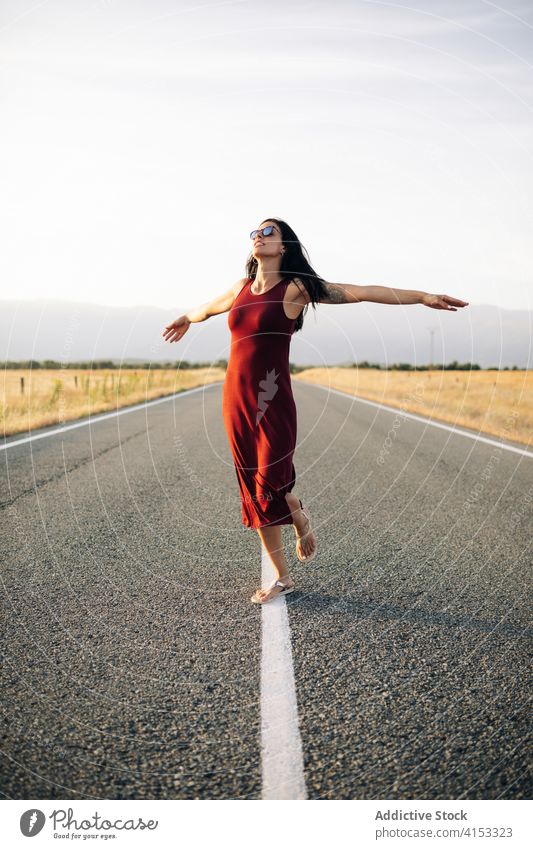 Content woman walking along road in summer carefree traveler enjoy vacation freedom smile female empty roadway dress sunhat trip happy holiday journey young