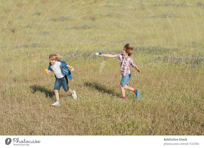 Content siblings playing in field together water gun pistol child brother having fun summer meadow positive joy cheerful grass weekend countryside nature run