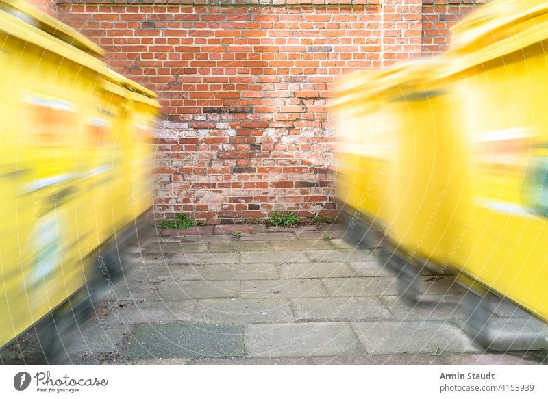 moving yellow dumpster in front of a red brick wall bin blur conservation container dustbin environment environmental fence garbage garden gate germany hdr
