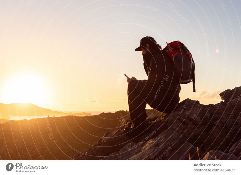 Male traveler browsing smartphone in mountains hiker man sunset watching admire using highland male rock cellphone device sit trekking journey adventure trip