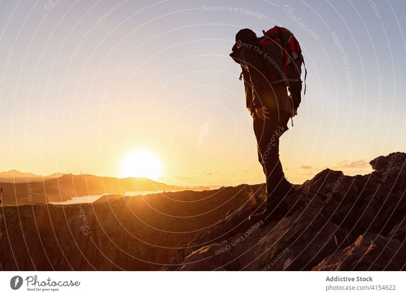 Male hiker with backpack in highland valley traveler hill man mountain admire stand explore sunset sky vacation sundown ridge landscape scenic rock majestic guy