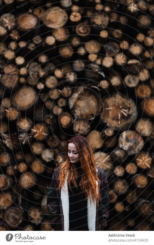 Woman in warm clothes standing near stacked wooden logs woman autumn season woodpile jacket travel young female countryside woodland germany austria resource
