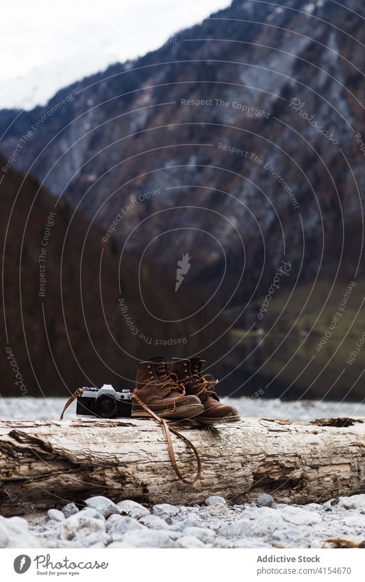 Boots and photo camera placed nearby on rocky waterfront in autumn day shore wooden boot adventure female photography carefree recreation cold travel tourism