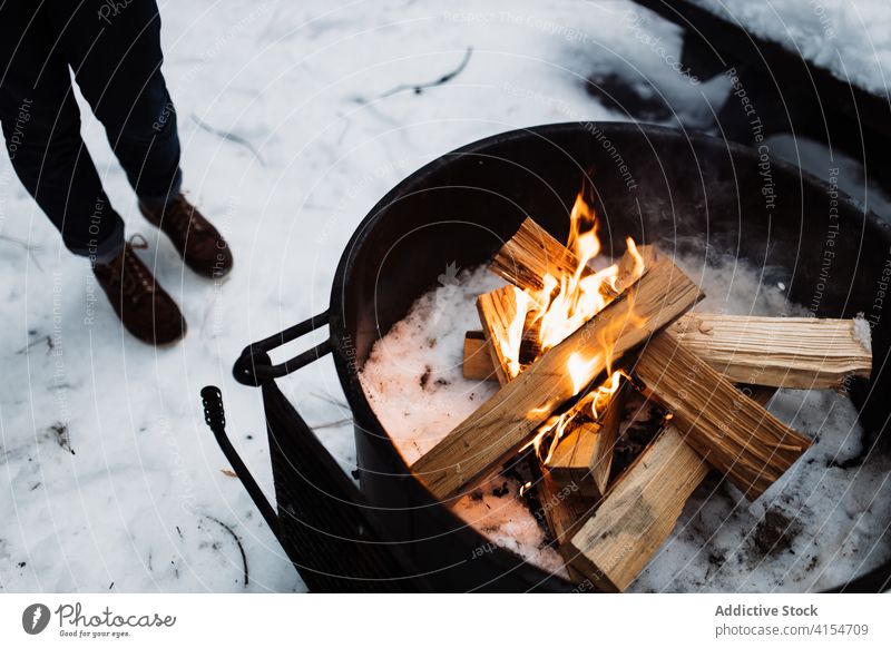 Anonymous person standing near bonfire in winter campfire firewood flame warm up traveler snow fireplace cold season adventure burn tourism usa united states