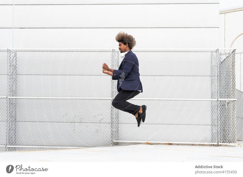 Stylish black man jumping near building in city businessman moment style entrepreneur manager carefree freedom male ethnic afro african american urban handsome