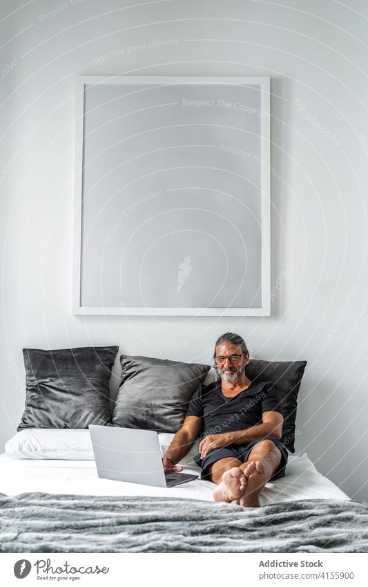Mature man on bed at home freelance remote work laptop typing mature entrepreneur using male browsing internet smile online project device gadget computer job