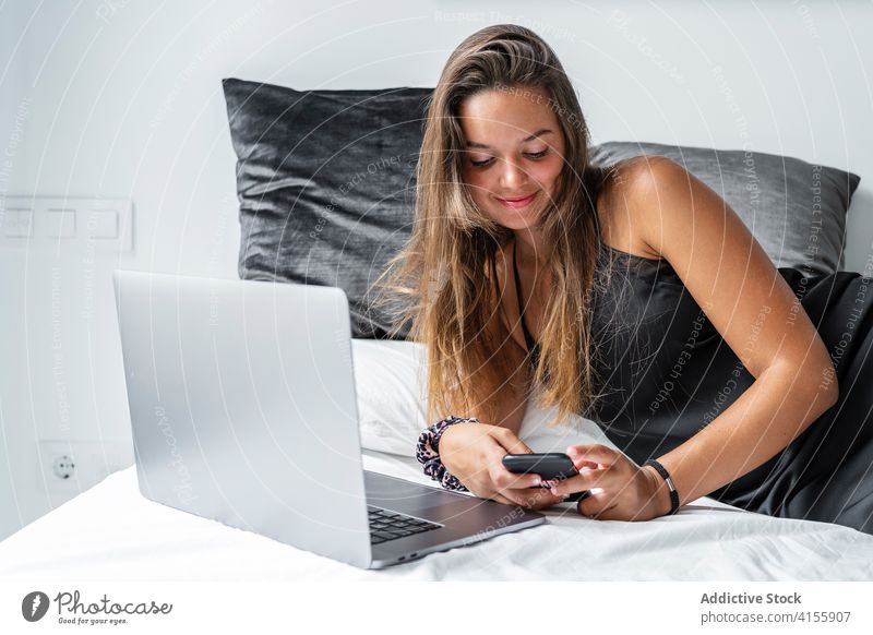 Content woman on bed in morning smartphone browsing sleepwear lazy lying bedroom using female nightwear rest soft comfort device gadget internet cozy happy