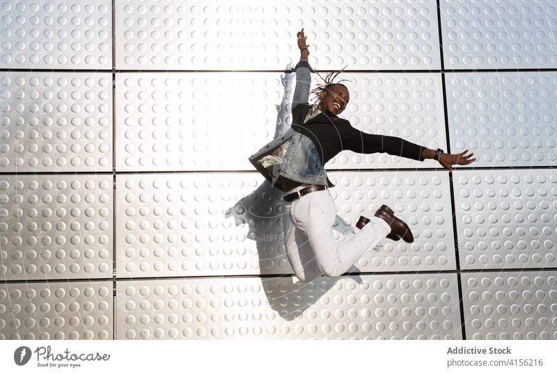 Stylish black man jumping near building in city businessman moment style entrepreneur manager carefree freedom male ethnic african american urban handsome smile