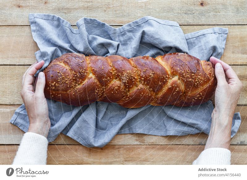 Person holding loaf of fresh braided bread on table baked seed whole food handmade rustic gastronomy tasty meal aromatic appetizing nutrition challah brioche