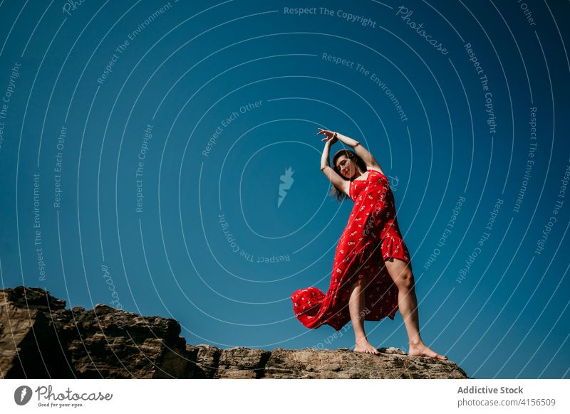 Graceful woman in dress on rocky hill grace red tender delight move slim female barefoot rough blue sky cloudless heaven nature serene sensual freedom carefree