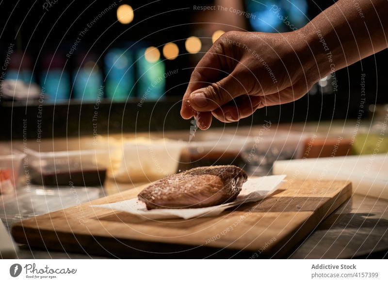 Appetizing slice of beef on wooden board in kitchen restaurant condiment cook add sprinkle meat chef food salt piece tasty gourmet fresh culinary spice