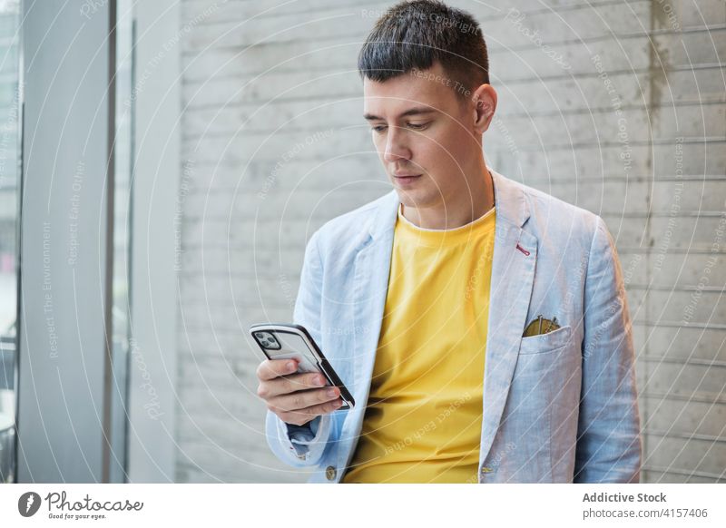 Man in trendy outfit using smartphone in office businessman style bright workplace serious workspace browsing male entrepreneur table lean cellphone surfing