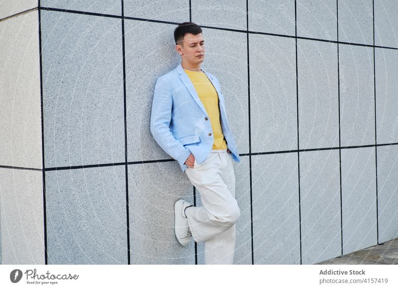 Young man on the street leaning on wall and looking down adult portrait background blue yellow male lonely minimal mood sense style think vintage depth creative