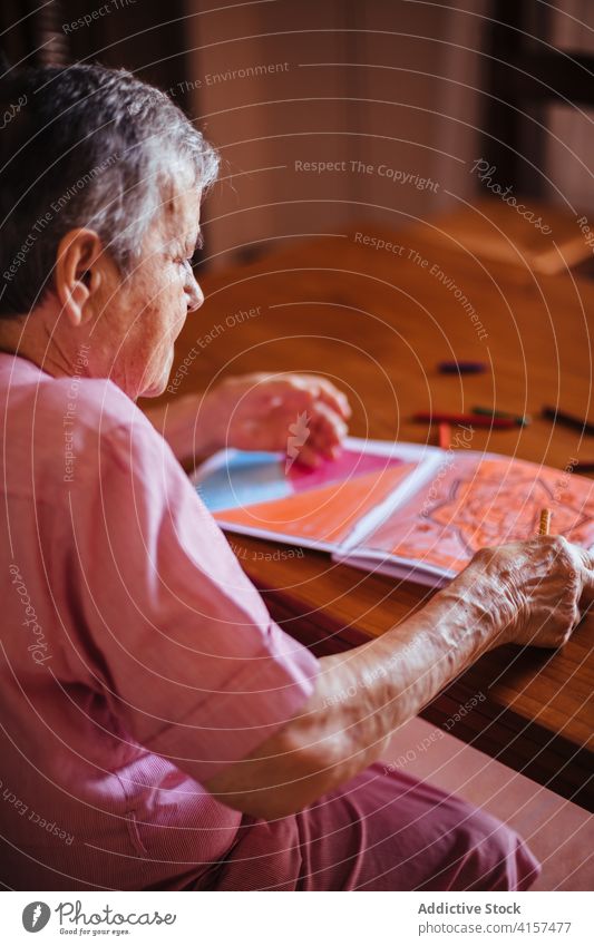 Older woman painting on a notebook old alzheimer mental health pencil retirement grandmother pensioner senior dementia female house elderly retired alone indoor