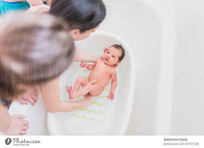 Anonymous parent and kid washing infant in basin baby water cry home care tender love child newborn clean bath bathroom unhappy displeased dissatisfied loud