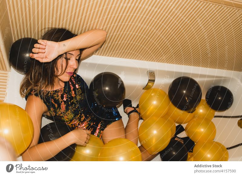 Young woman in bathtub with balloons after party sleep tired festive celebrate holiday event young female funny rest occasion xmas drunk color new year