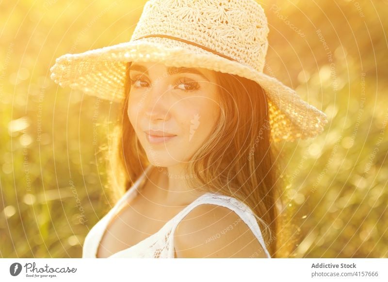 Charming woman in field in summer sunhat meadow sunset evening tender carefree relax female stand smile nature enjoy cheerful romantic rest sundown peaceful