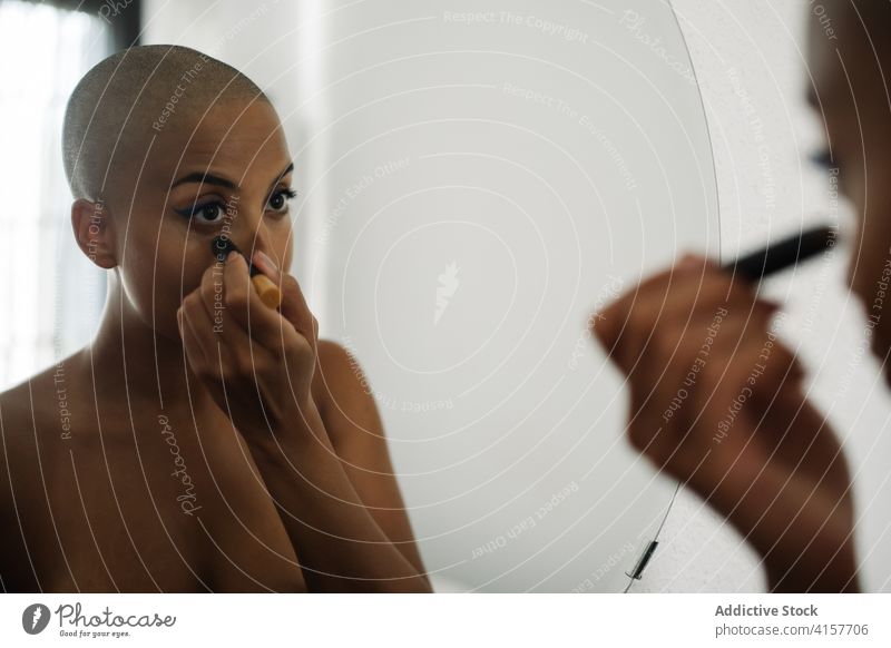 Serious black woman doing makeup at home visage apply applicator brush mirror reflection female ethnic african american bald hairstyle appearance beauty liquid