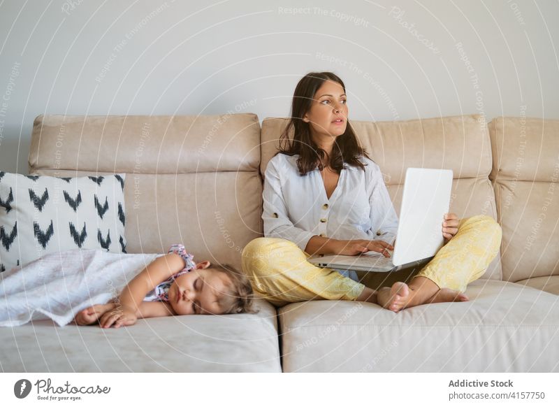 Distracted woman working on the sofa with the laptop while a toddler is sleeping on a side tranquility maternity responsibility tenderness dreaming motherhood