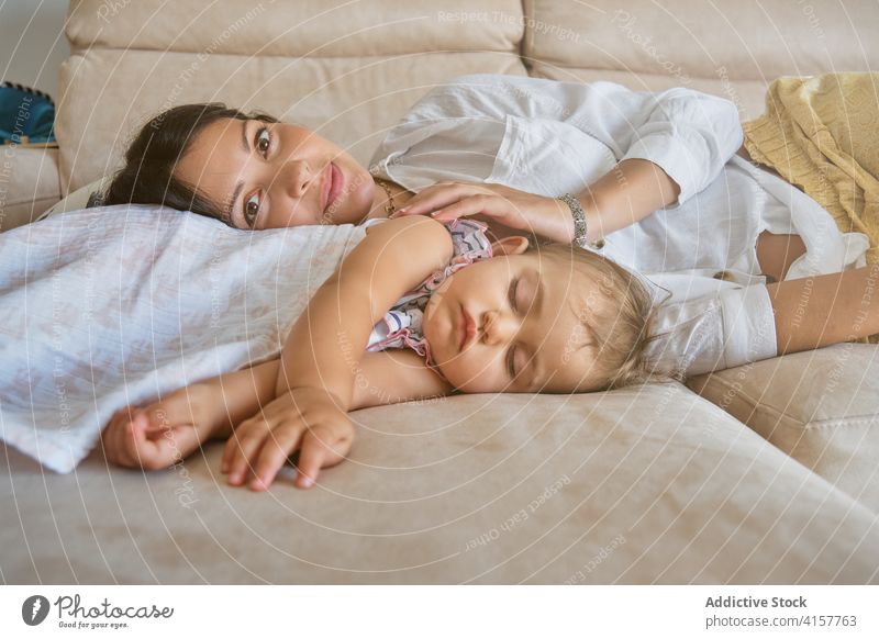 Woman facing the camera while lying on the sofa next to a sleeping toddler exhausted caressing trust affection embrace feeling infant motherhood tenderness