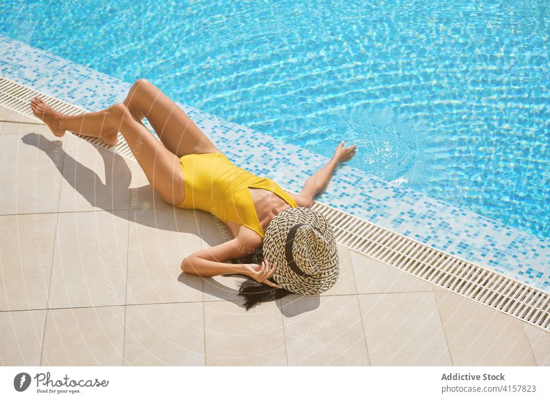 Slim woman in hat sunbathing at poolside summer lying chill enjoy resort relax rest female slim leisure tourist suntan wellness wellbeing travel tourism