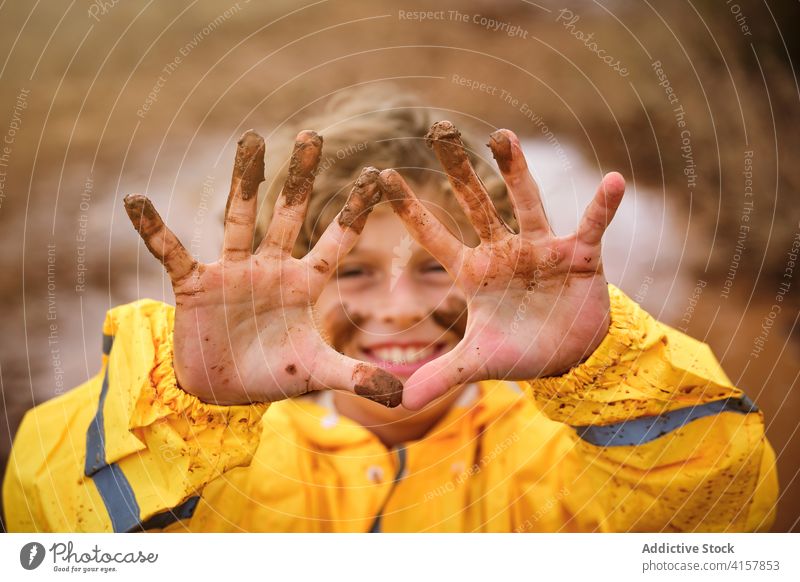 Selective focus on the muddy hands of a child with a muddy face in raincoat outdoors joke pride infant messy spiritual playful fingers mark ethnic storm curly