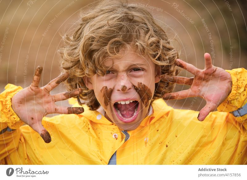 Portrait of a boy with a muddy face showing his dirty hands with an angry expression joke infant messy playful fingers mark ethnic curly gesture makeup problem