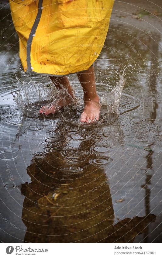 Barefoot child in a yellow raincoat jumping into a puddle splashing water barefoot enjoyment wet fly weather play protection drop game children funny motion