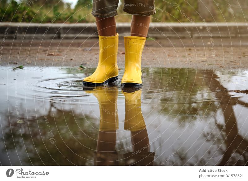 Legs of a boy with yellow rain boots in a puddle water in a path lifestyles messy stand kids wet weather joy play drop reflection children symmetry legs mirror