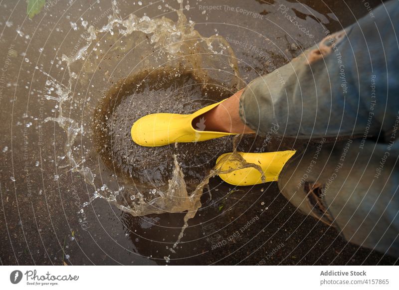 Aerial view of the yellow rain boots hitting a puddle splashing water step joke innocence lifestyles messy aerial playful kids enjoyment wet weather drop