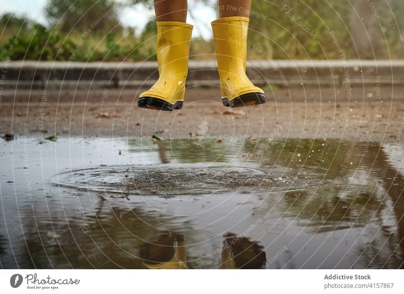 Legs of a boy with yellow rain boots jumping above a puddle water in a path joke innocence lifestyles messy playful splashing kids enjoyment wet weather drop
