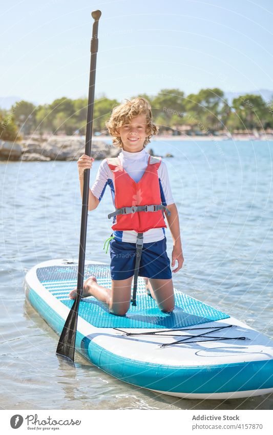 Boy kneeling on a paddleboard in the sea individuality rescue surfing protect safe confidence balance enjoyment fit recreation relaxation hobby expression smile