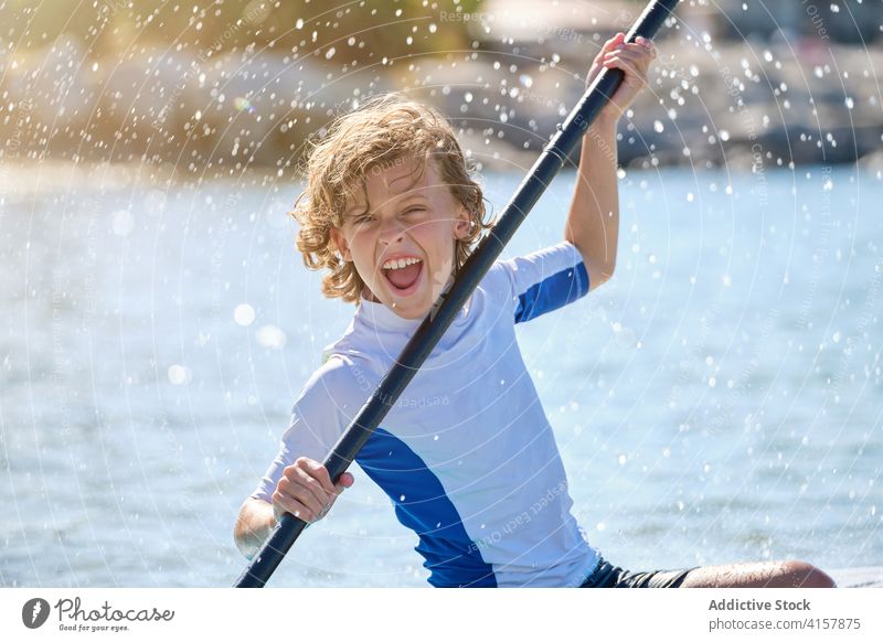 Portrait of a boy on a paddle surfboard playing with the paddle vitality gesture splash laugh sit raise wear balance win enjoy recreation floating model relax