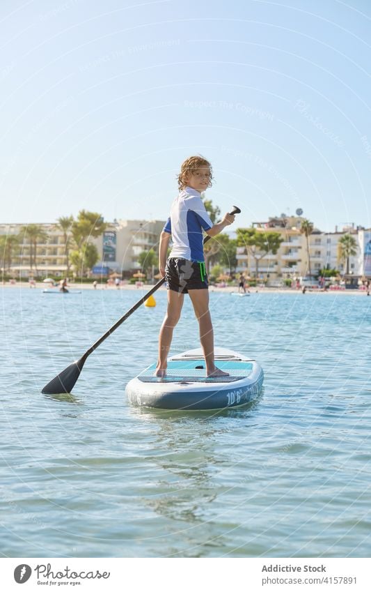 Boy rowing in a paddle surfboard while turning back to look at the camera on the sea lifestyles effort move practice surfing trend attention splash balance