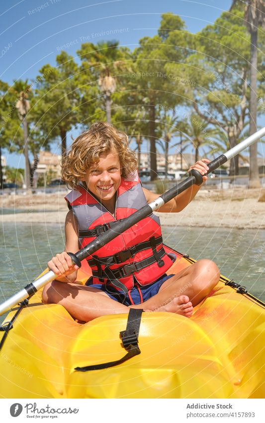 Boy with a life jacket rowing and facing the camera in a kayak in the sea experience move safe weekend joyful dangerous pleasure recreation protection smile